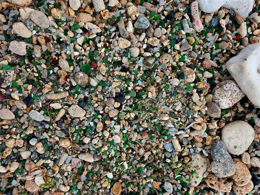 Close-up of green, white and brown sea glass mixed with pebbles on the shore