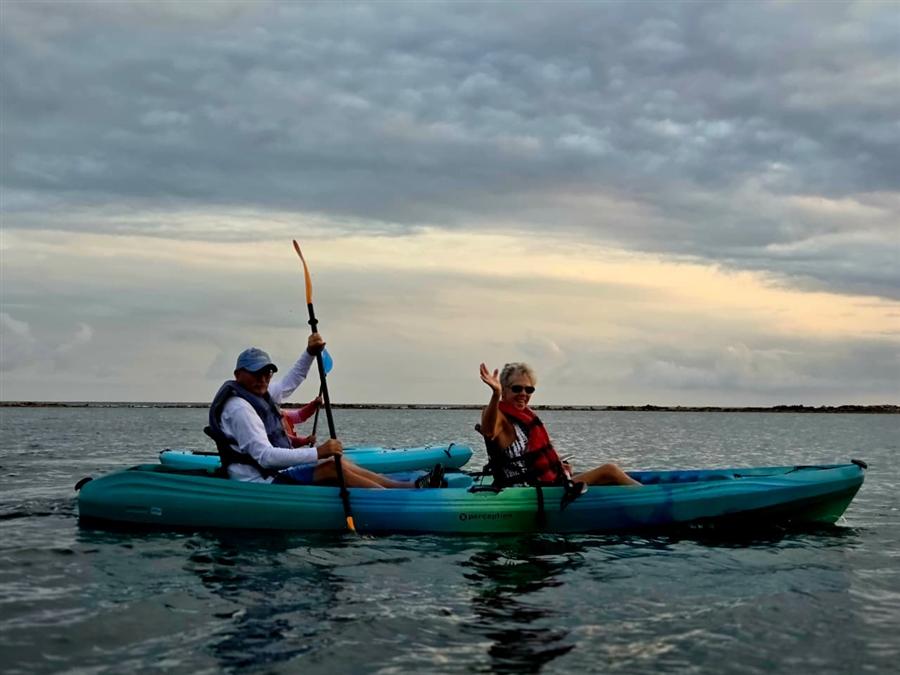 Couple waving from a turquoise kayak on calm water